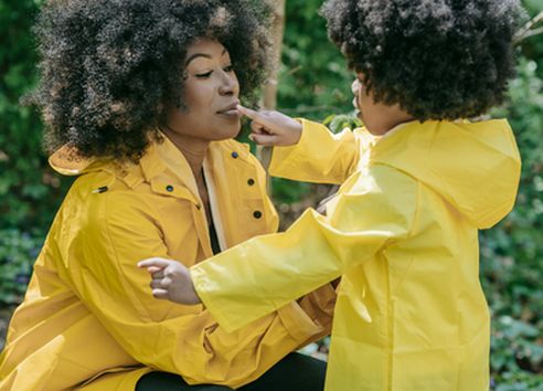 Woman with afro and child both in yellow rain coats in woods