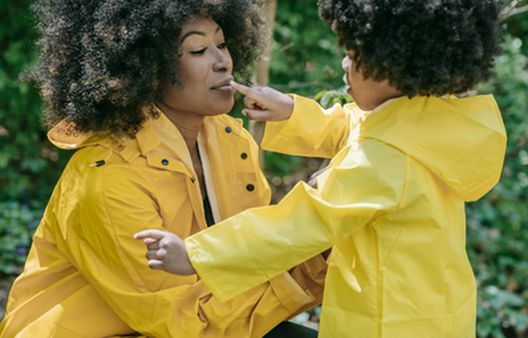 Woman with afro and child both in yellow rain coats in woods