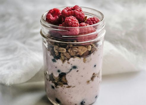 Healthy overnight oats recipe in a glass jar with chia seeds, granola and fresh raspberries for an easy make-ahead breakfast.