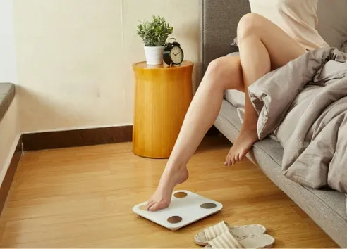 Woman's feet stepping on scales in bedroom