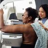 Asian female technician positions an African-American woman at an imaging machine to receive a mammogram.