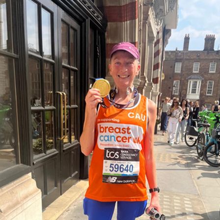 Woman in pink hat and orange breast cancer uk running vest holding a gold medal