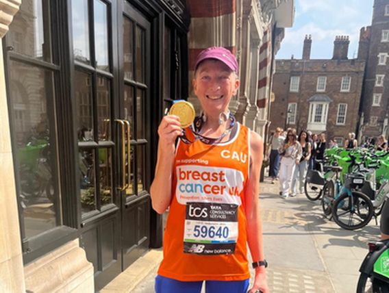 Woman in pink hat and orange breast cancer uk running vest holding a gold medal