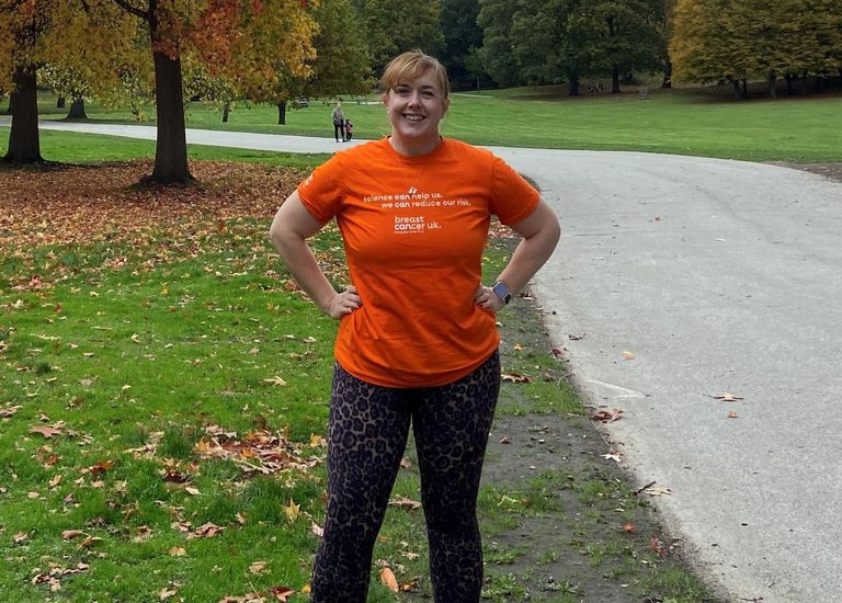 Woman standing in park in orange shirt with hands on hip