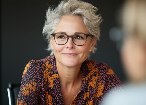 Woman with short blonde hair and glasses smiling with floral shirt on