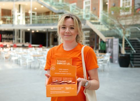 Blonde woman standing with orange charity collection box wearing orange breast cancer uk t-shirt