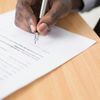 Person signing white paper document on brown table