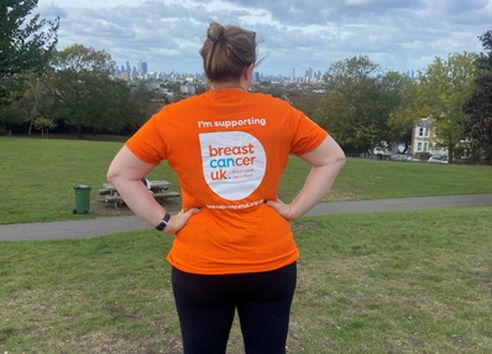 Woman with back to camera with orange Breast Cancer UK logo tshirt on in field