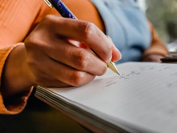 a person in orange jumper using pen to make notes on notepad
