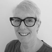 Woman in black and white headshot smiling at camera with shirt white hair and black rimmed glasses onElspeth Mackeggie Gurney