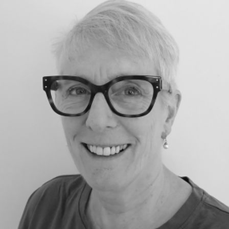 Woman in black and white headshot smiling at camera with shirt white hair and black rimmed glasses onElspeth Mackeggie Gurney