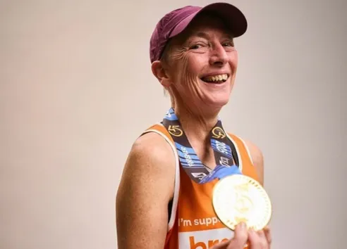 Female London marathon runner in Breast Cancer UK running vest holding medal