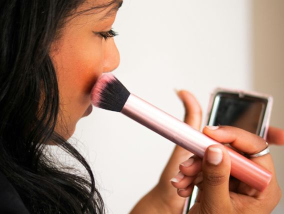 woman using makeup brush in compact mirror