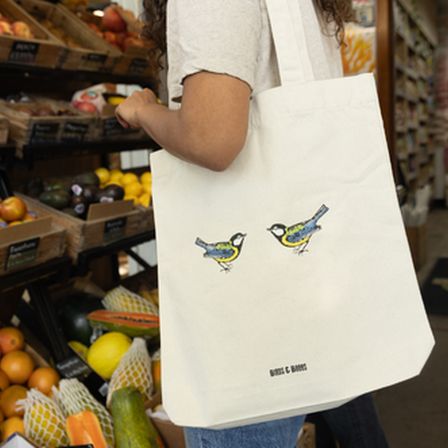 Woman in front of a fruit stand holding a tote bag with birds on