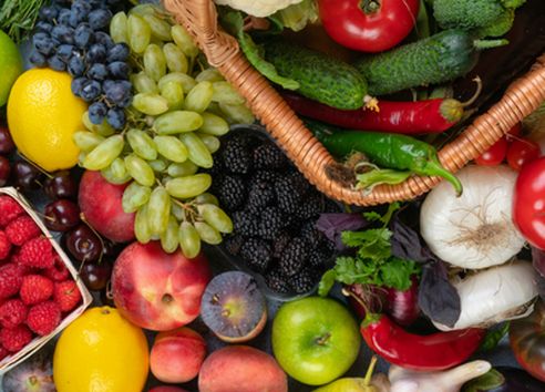 Wide variety of fresh fruit and vegetables spread across a flat lay, including berries, stone fruit, tomatoes, and green vegetables for a balanced diet