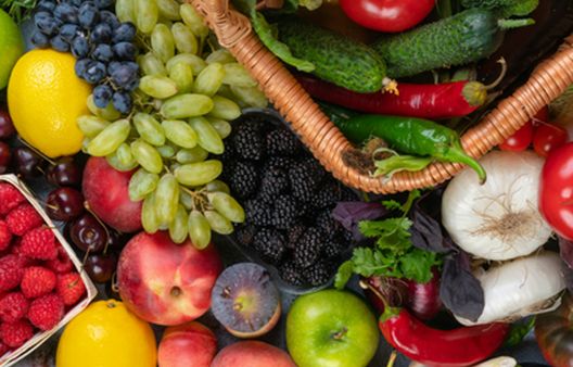 Wide variety of fresh fruit and vegetables spread across a flat lay, including berries, stone fruit, tomatoes, and green vegetables for a balanced diet