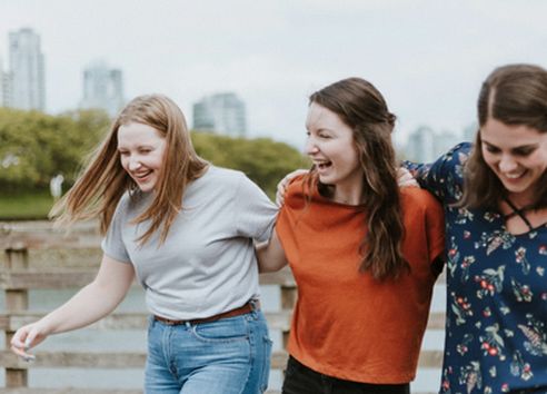Three young adult women walking with linked arms and laughing