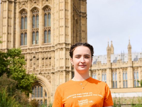 Brunette woman wearing orange breast cancer uk t-shirt standing in front of parliment