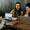 Three people at table on their laptops laughing