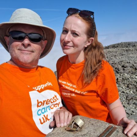 two people in orange t-shirts at top of mountain taking a selfie Smiling
