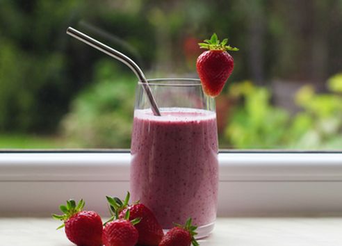 Red berry smoothie in glass on windowsill with strawberries scattered around