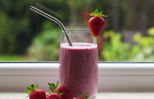 Red berry smoothie in glass on windowsill with strawberries scattered around