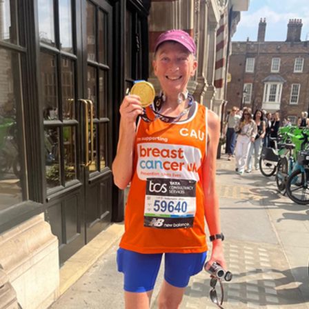 Woman with orange running vest on smiling in street with purple cap holding gold medal