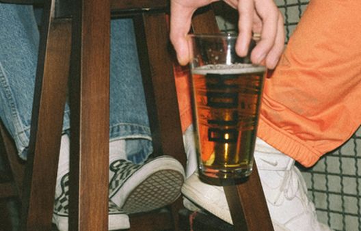 Person holding class of alcohol on stool with orange trousers on