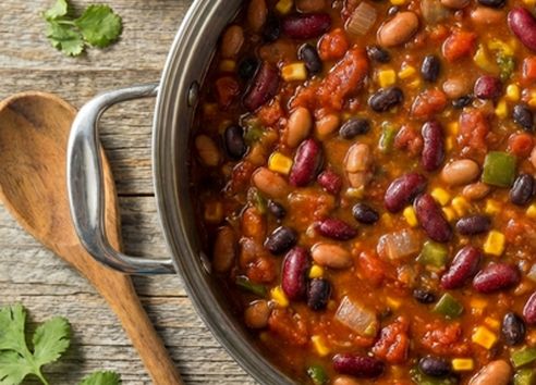A pot of hearty three bean chili on a wooden kitchen worktop