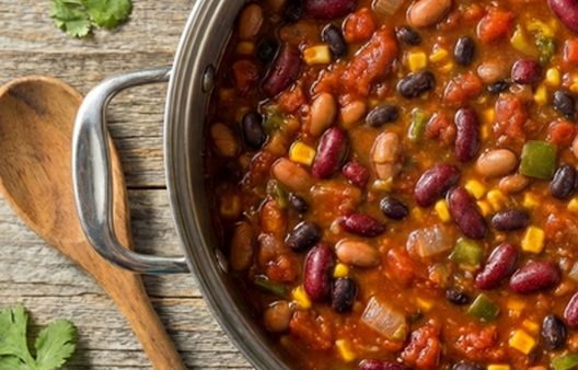 A pot of hearty three bean chili on a wooden kitchen worktop