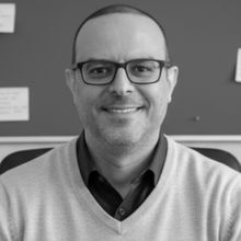Man with shaved head in black and white head shot smiling at the camera in v neck jumper and glassesProfessor Mohamed Abdallah