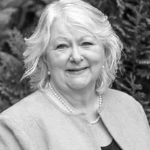 Woman with short blonde hair and pearls round neck smiling at camera in black and white headshotJulie Toben