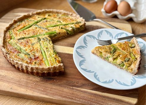 Savoury asparagus quiche on a wooden board with a sliced portion served on a plate.