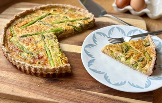 Savoury asparagus quiche on a wooden board with a sliced portion served on a plate.