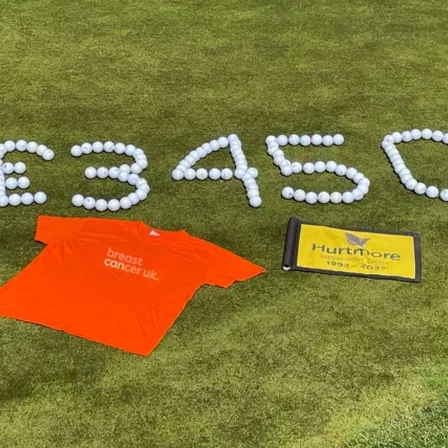 orange tshirt laid in front of golf balls set into amount of money on golfing green