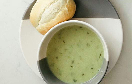 Homemade watercress soup recipe served in a grey bowl with a crusty bread roll on a white surface